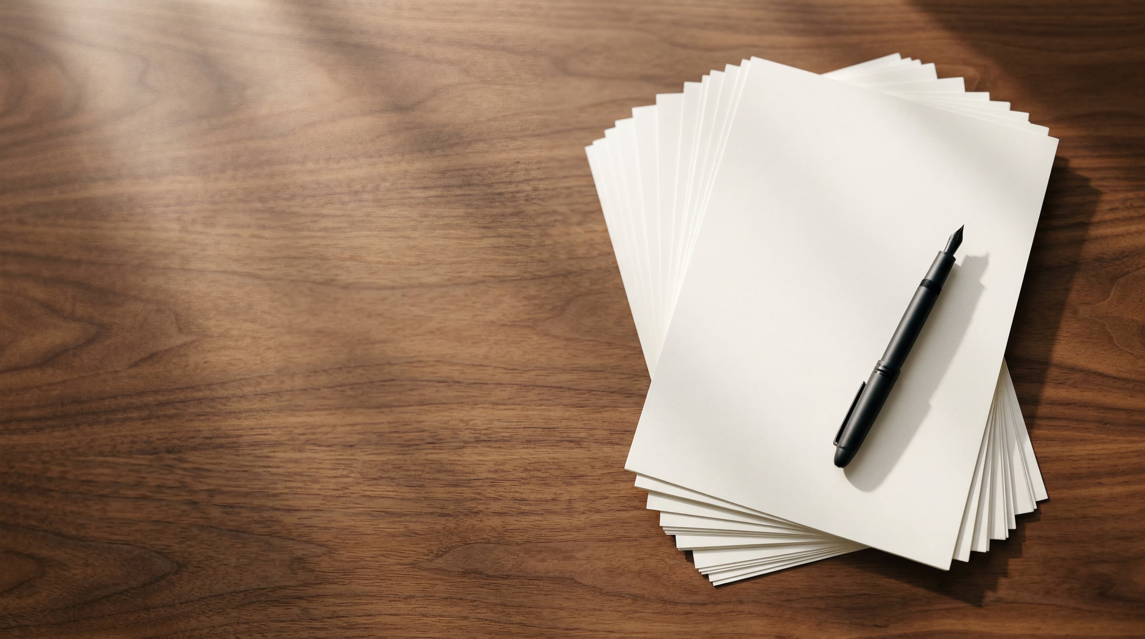 A neatly fanned stack of unmarked white press-release sheets on a polished walnut desk beside a slim matte-black fountain pen, soft directional sunlight.